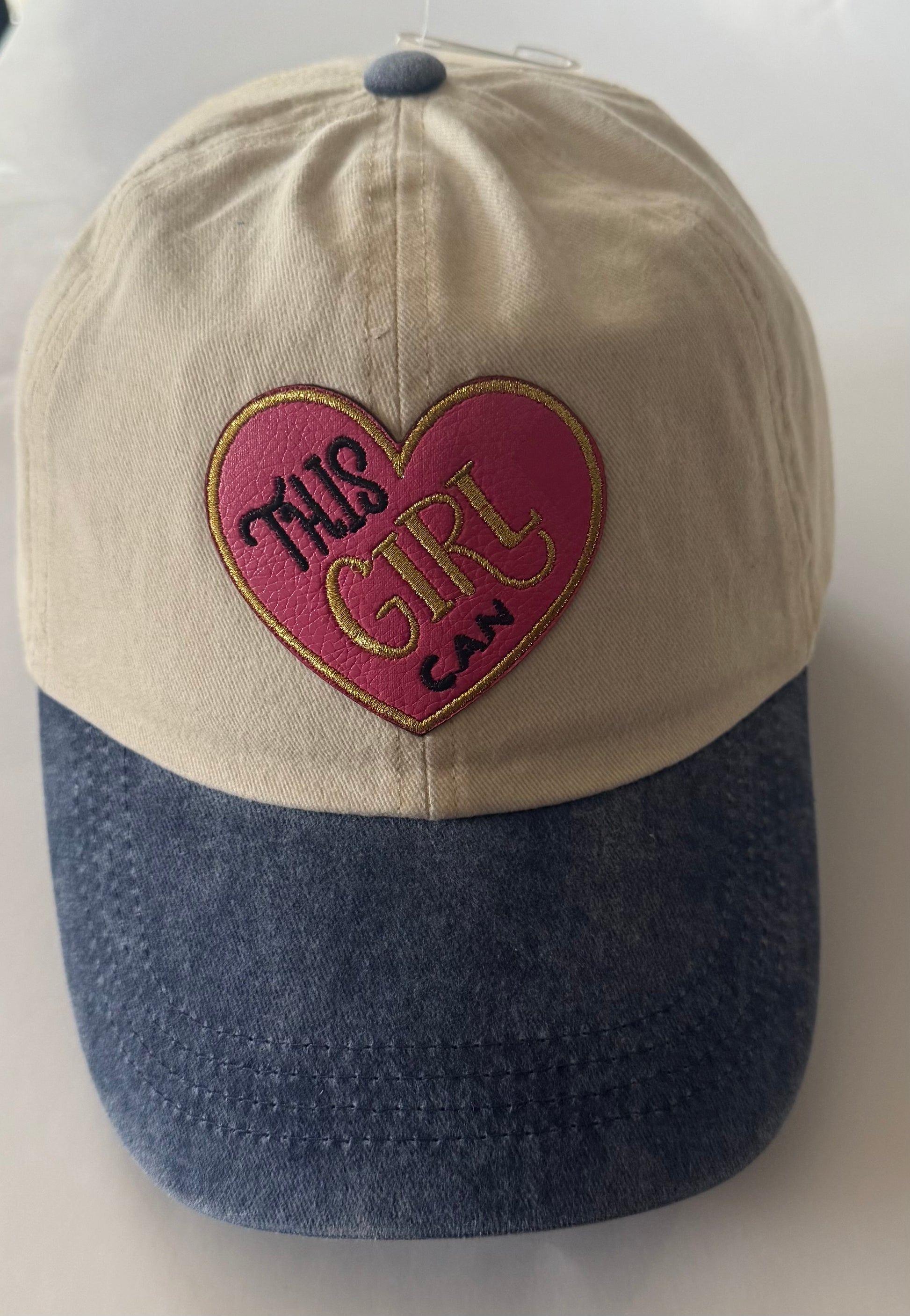 Tan cap with denim blue bill, all cotton with pink and gold heart shaped "This Girl Can" patch on the front. Cap has adjustable strap in the back. Denim button on the top of the cap.