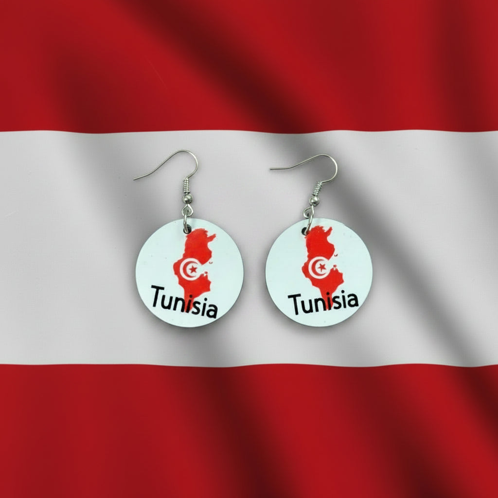 Pair of circular earrings featuring Tunisia’s map outline in red with a white crescent and star emblem and the word “Tunisia” printed below, displayed on a red and white surface. Roxzell