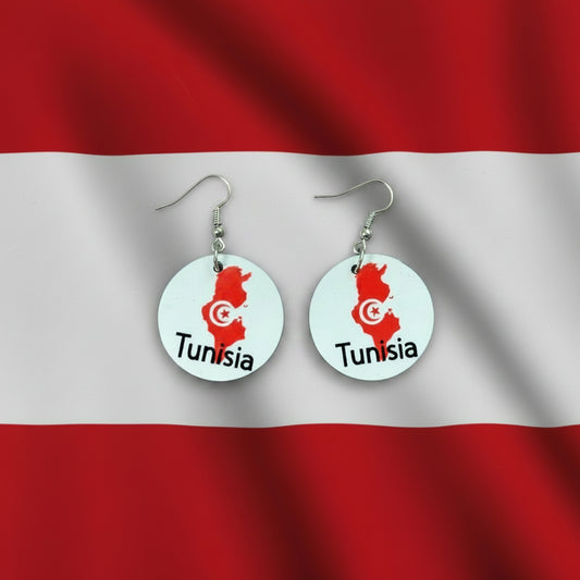 Pair of circular earrings featuring Tunisia’s map outline in red with a white crescent and star emblem and the word “Tunisia” printed below, displayed on a red and white surface. Roxzell