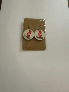 Tunisia map earrings attached to a brown backing card inside a clear plastic sleeve, showing red map designs with crescent and star symbols and “Tunisia” text. Roxzel