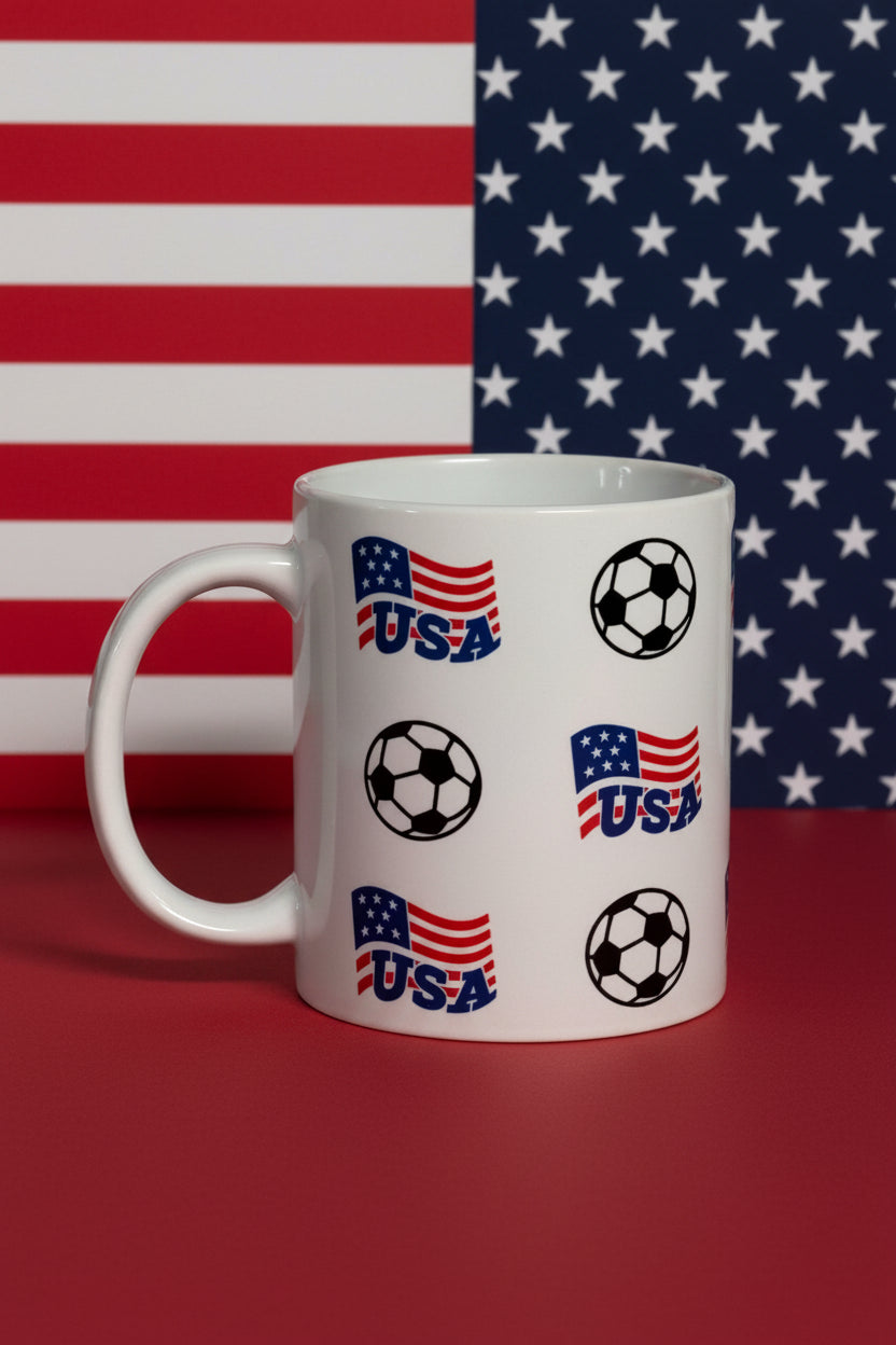 White ceramic mug featuring red, white, and blue USA flag graphics with bold “USA” text and black‑and‑white soccer ball pattern.