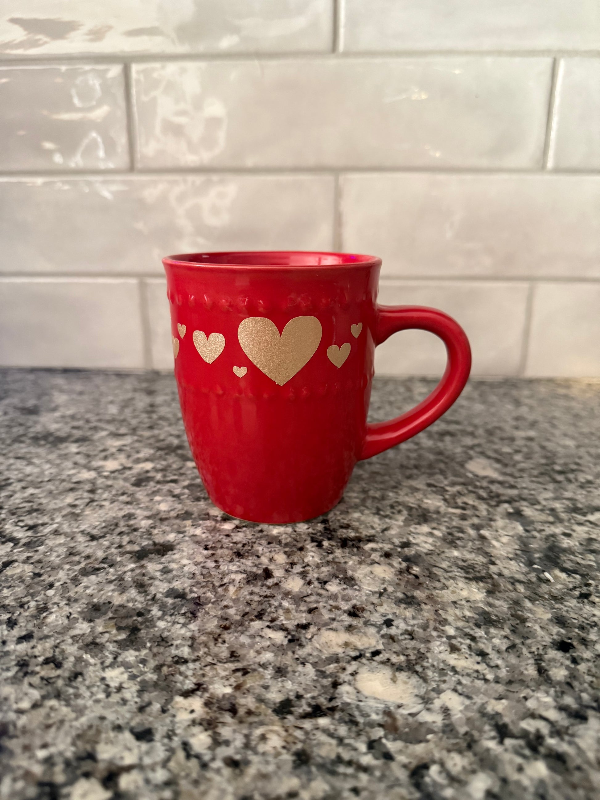 Red mug with gold heart designs on a gray countertop, Roxzell