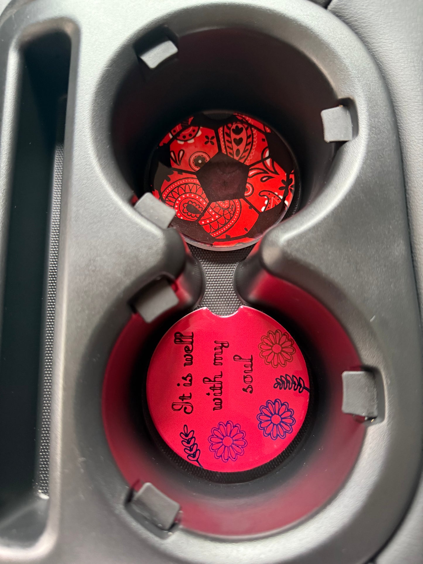 Two red car coasters with patterns in a cup holder.
