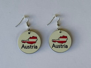 Pair of earrings featuring Austria’s map outline filled with red and white flag colors and the word “Austria” printed below, displayed on a wooden surface.