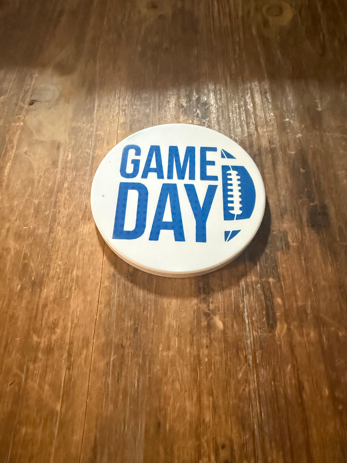 White coaster with blue “GAME DAY” text and football graphic replacing the letter D, placed on wooden surface. Roxzell