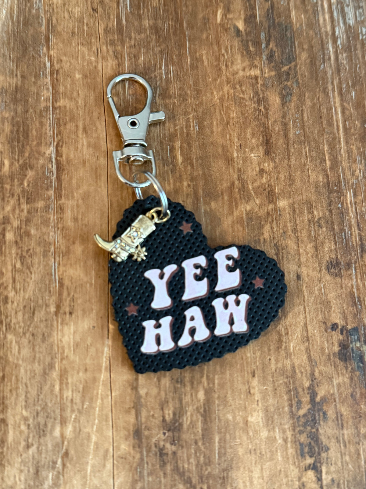 Black heart bag charm with pale pink Yee Haw lettering, brown stars, dangling cowboy boot charm, and silver-tone clasp. Roxzell