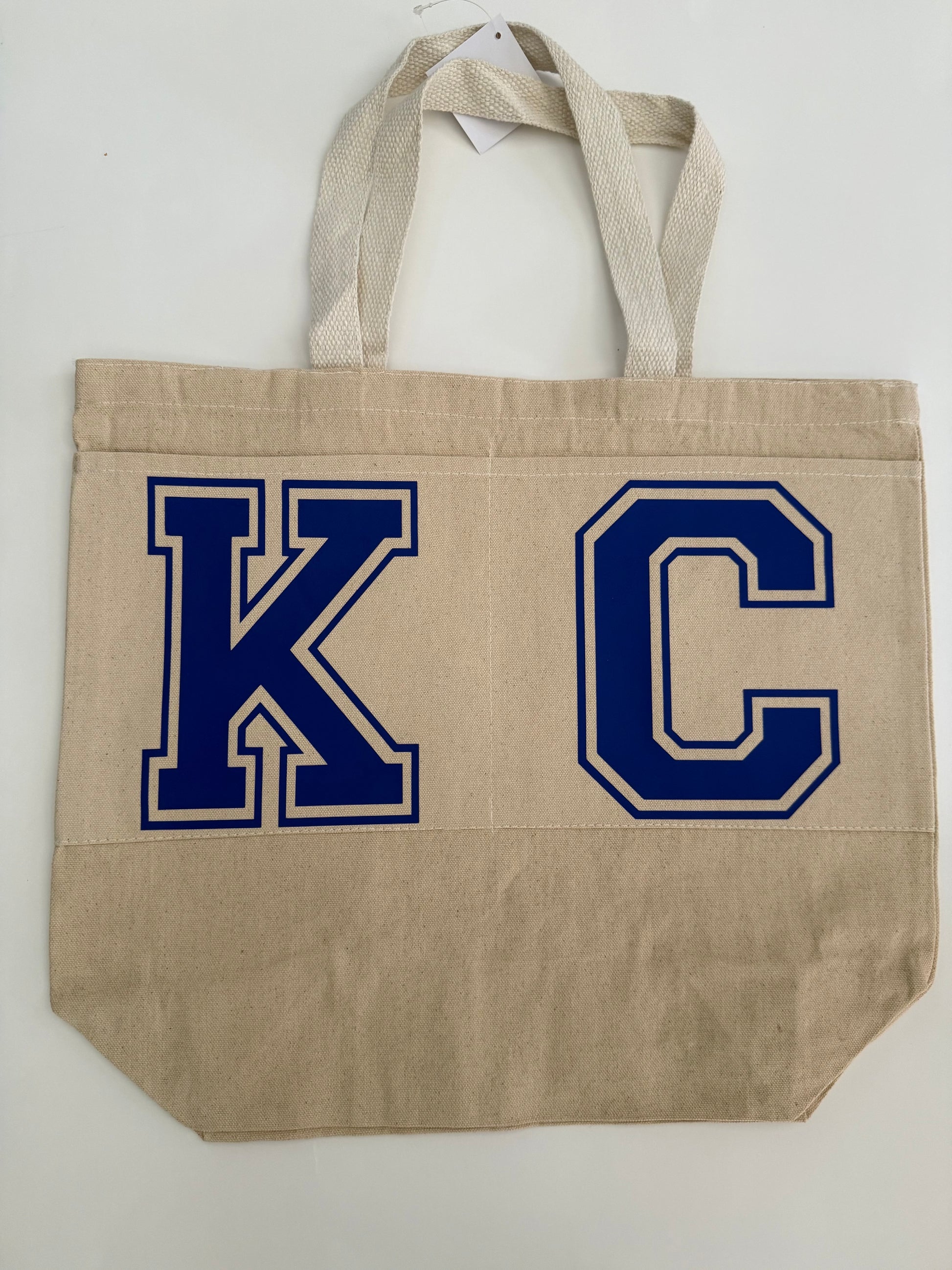 Beige cotton canvas tote bag with bold blue “KC” lettering shown on the front. Roxzell