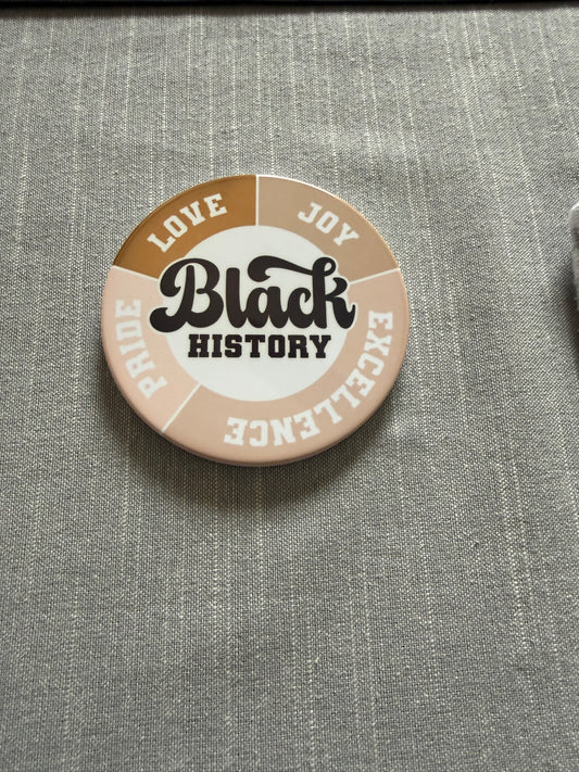Circular Black History coaster with bold Love, Joy, Pride, and Excellence text and colored segments on gray fabric