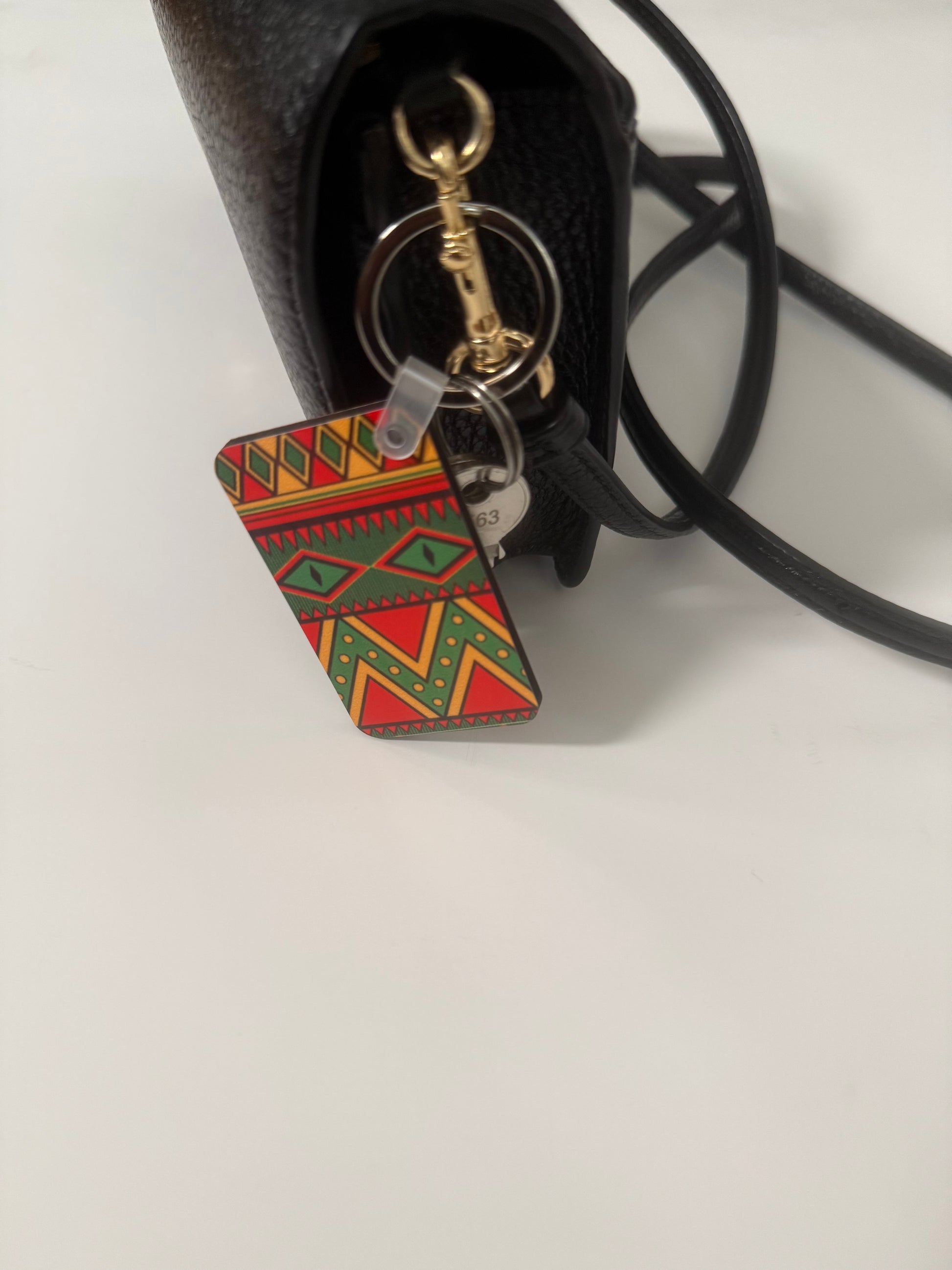 Geometric patterned black history themed keychain hanging from a black handbag with gold hardware.