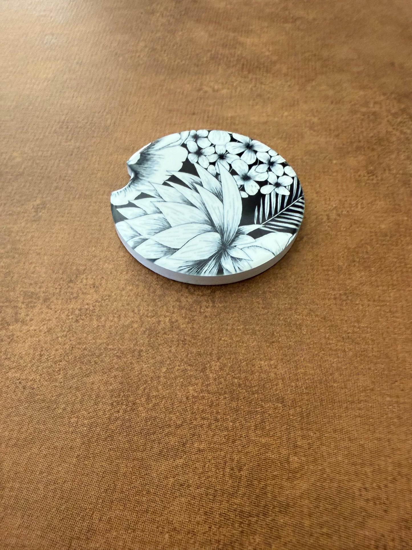 Round car coaster with intricate black and white floral pattern on textured brown surface, Roxzell