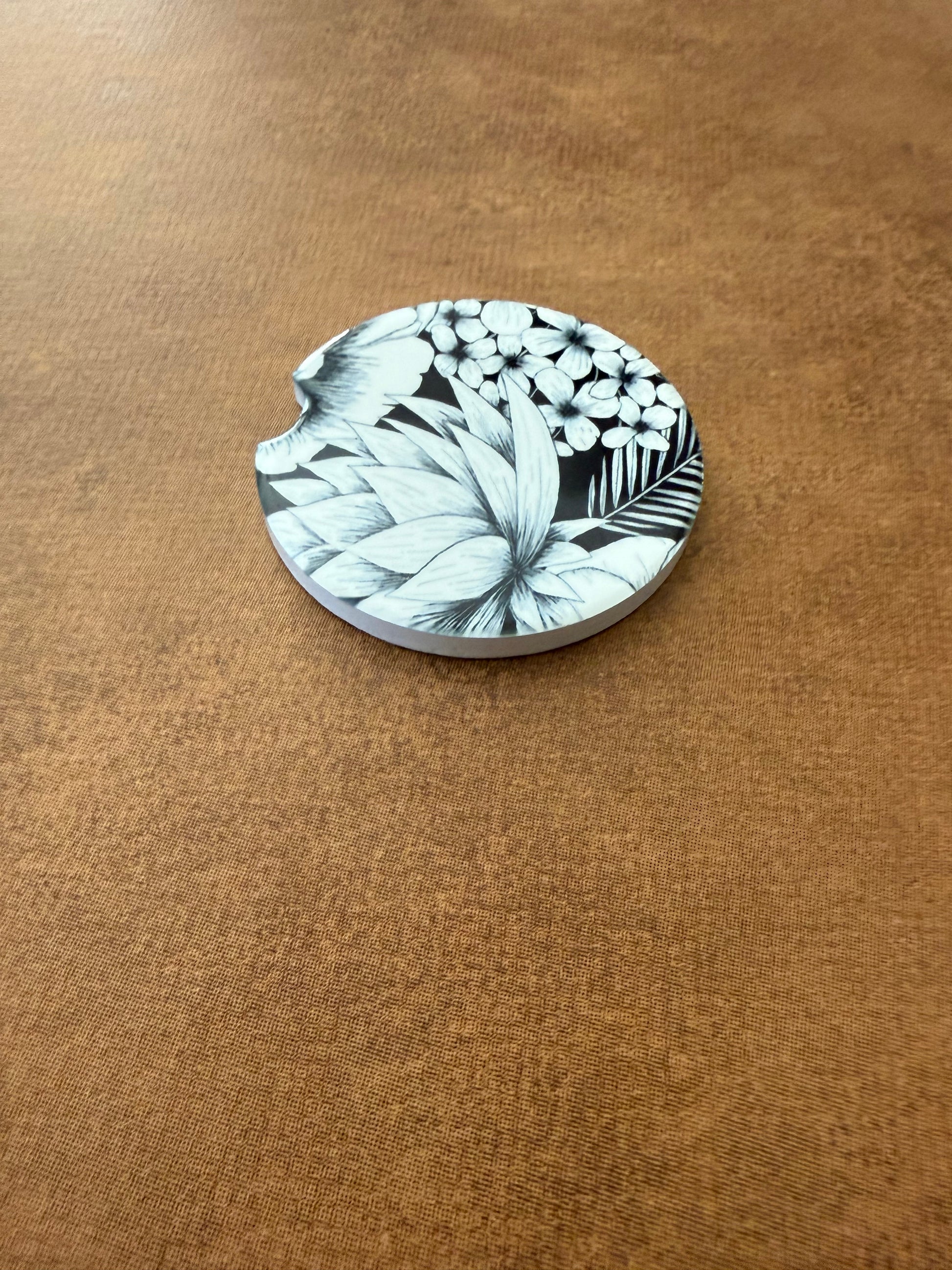 Round car coaster with intricate black and white floral pattern on textured brown surface, Roxzell