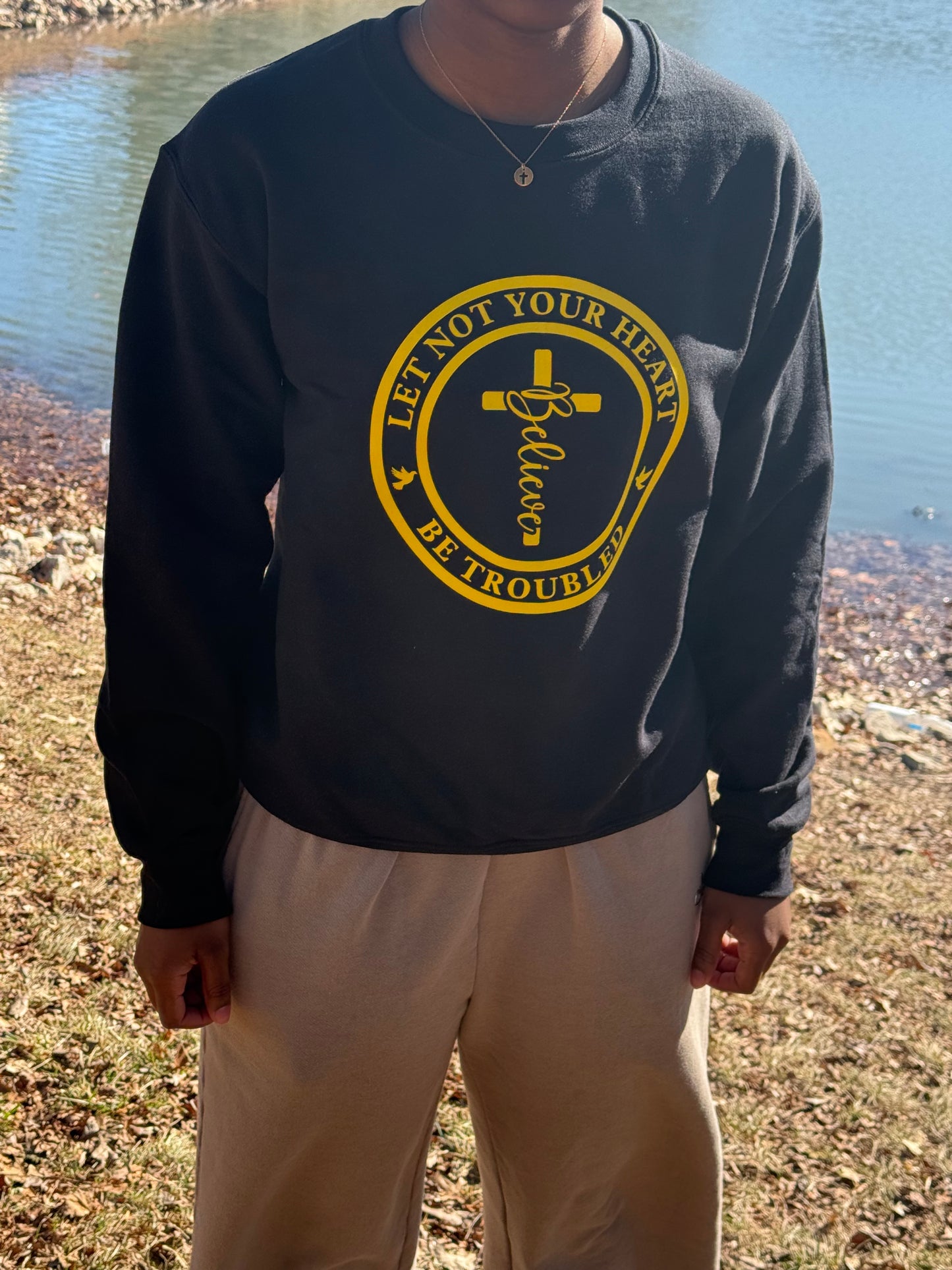Person wearing a black sweatshirt with Let Not your Heart be Troubled design with cross necklace, showcasing faith-inspired outfit, Roxzell