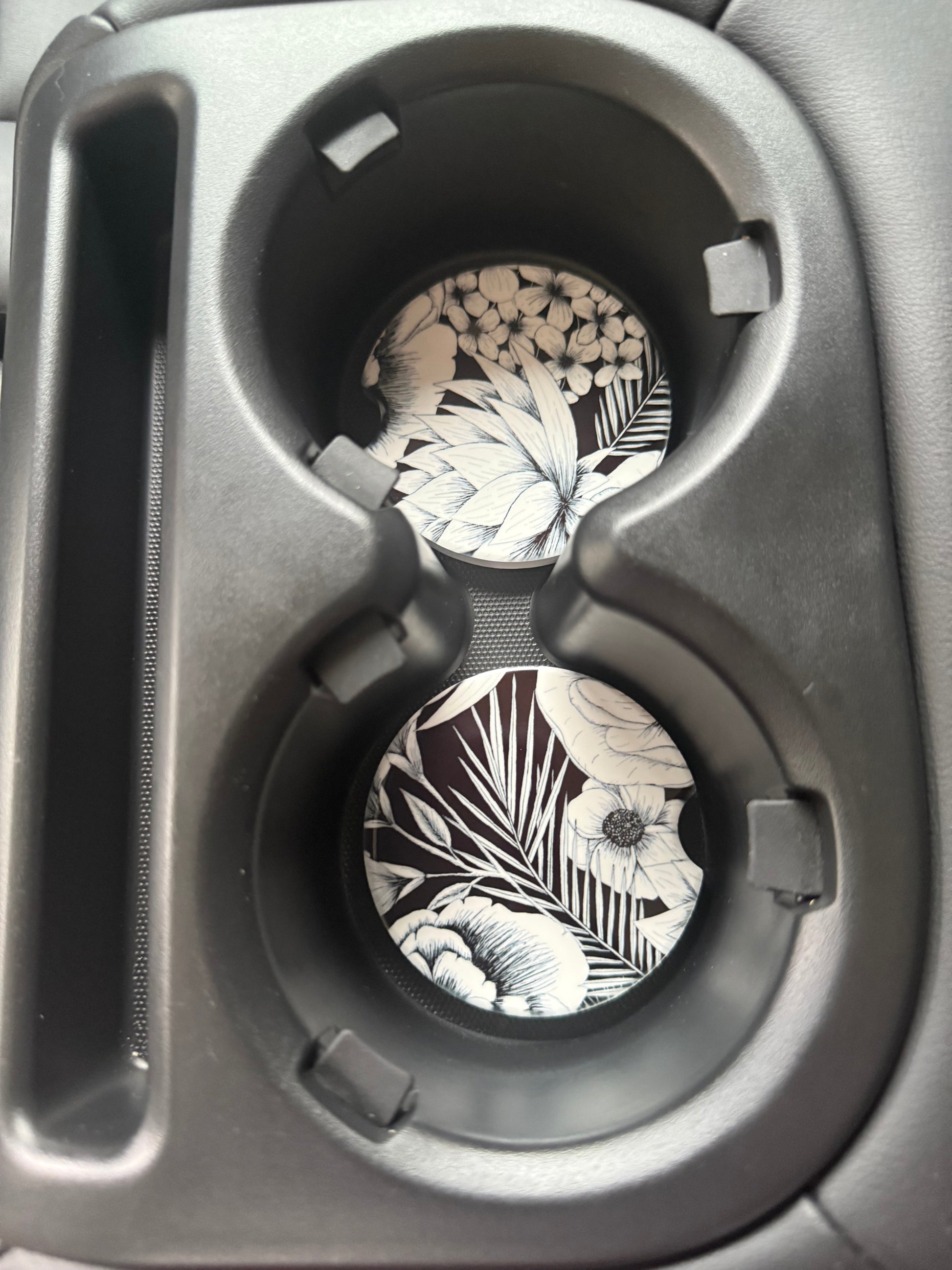 Two classic round car coasters with black and white flower design in a car cupholder, perfect for stylish gifting, Roxzell