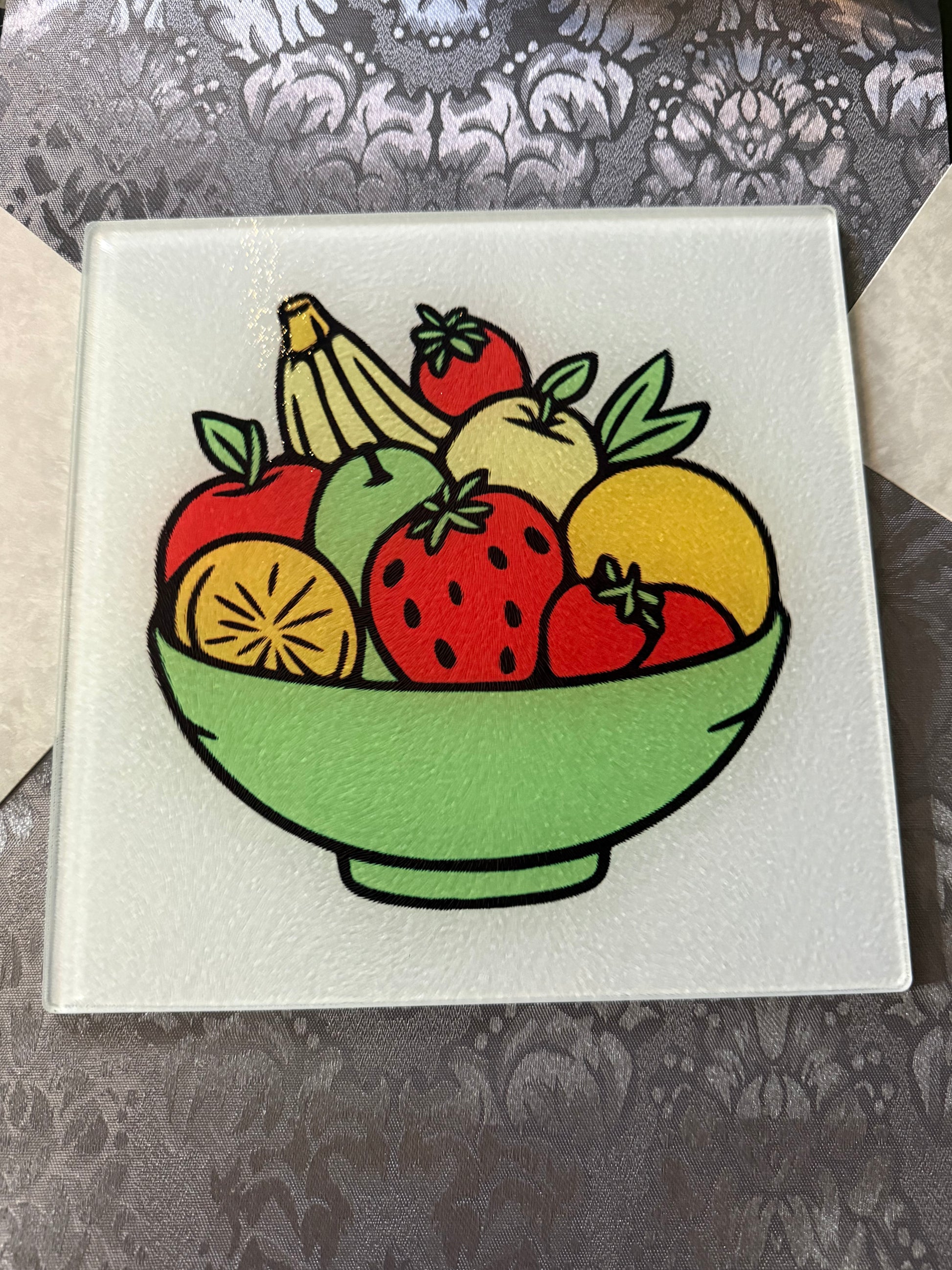 Tempered glass cutting board featuring a vibrant multicolor fruit illustration on a kitchen table with a gray table runner, Roxzell