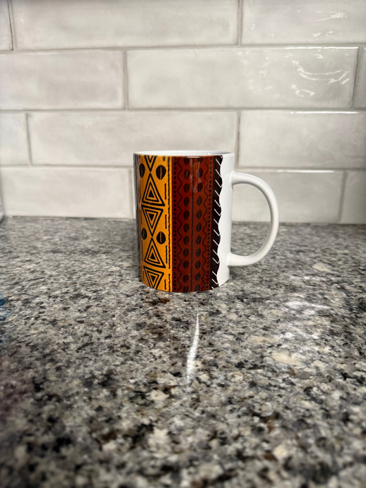 Side angle of a ceramic mug featuring layered tribal-inspired designs in orange, brown, and black on a granite countertop. Roxzell