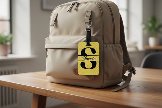 Yellow letter "S" and name "Sherrie" luggage tag on a beige backpack on a table, Roxzell