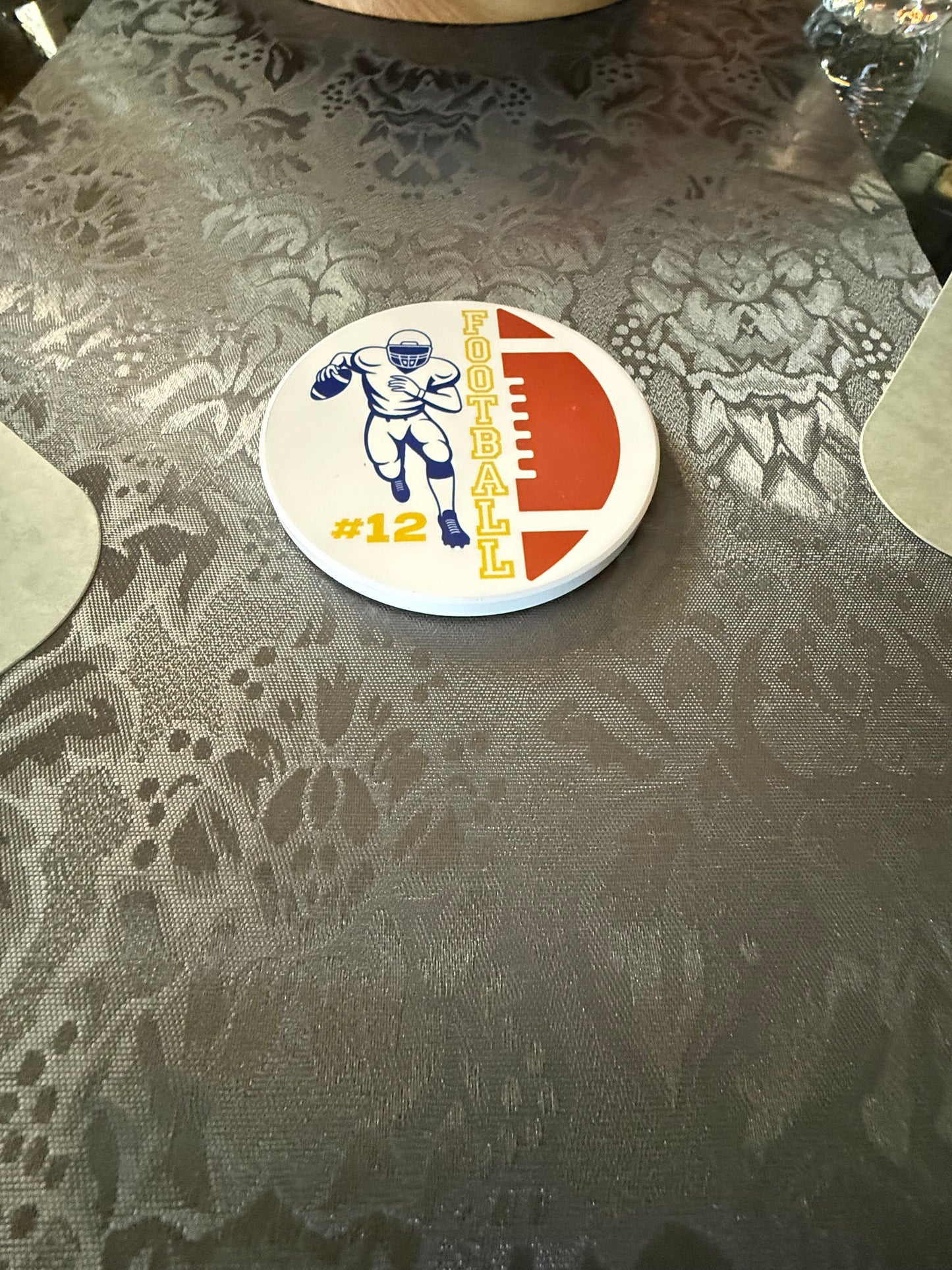 Sports themed drink coaster with football player running and yellow FOOTBALL text and personalized #12 on a gray table runner, Roxzell