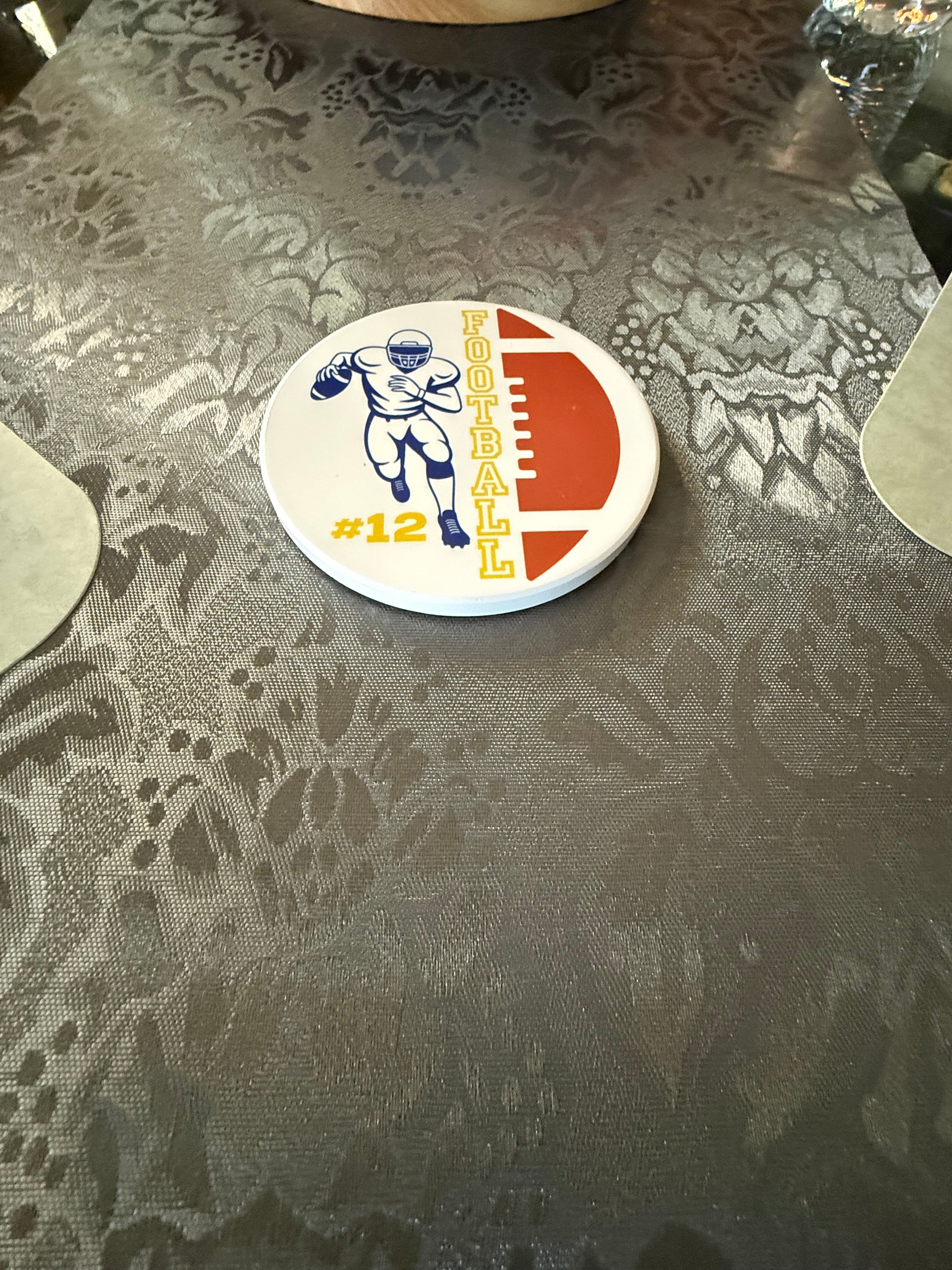 Sports themed drink coaster with football player running and yellow FOOTBALL text and personalized #12 on a gray table runner, Roxzell