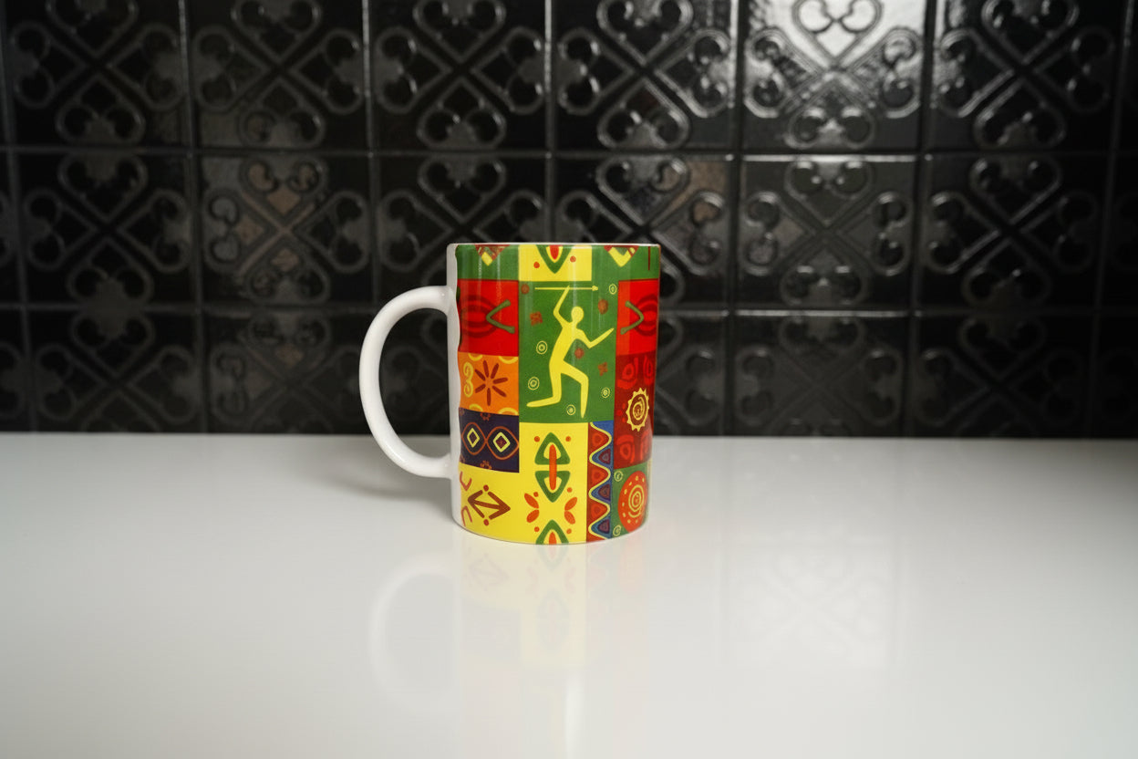 Close‑up of a ceramic mug featuring colorful geometric and symbolic patterns in red, yellow, green, and blue on a white counter with a black backsplash. Roxzell
