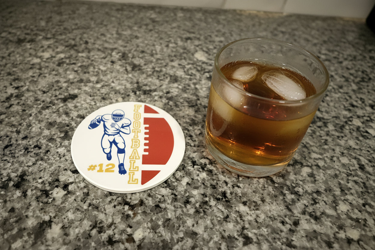 personalized football coaster featuring a brown ball and football player in blue uniform with #12 beside a glass of tea on a granite countertop, Roxzell