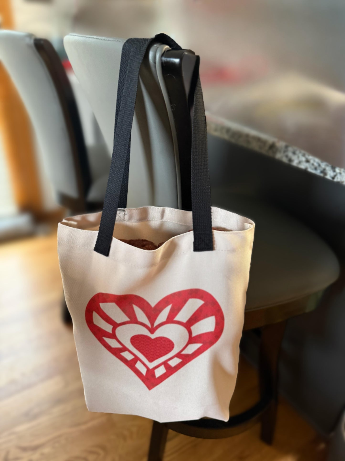 Beige tote bag with bold red geometric heart design hanging on a chair, Roxzell