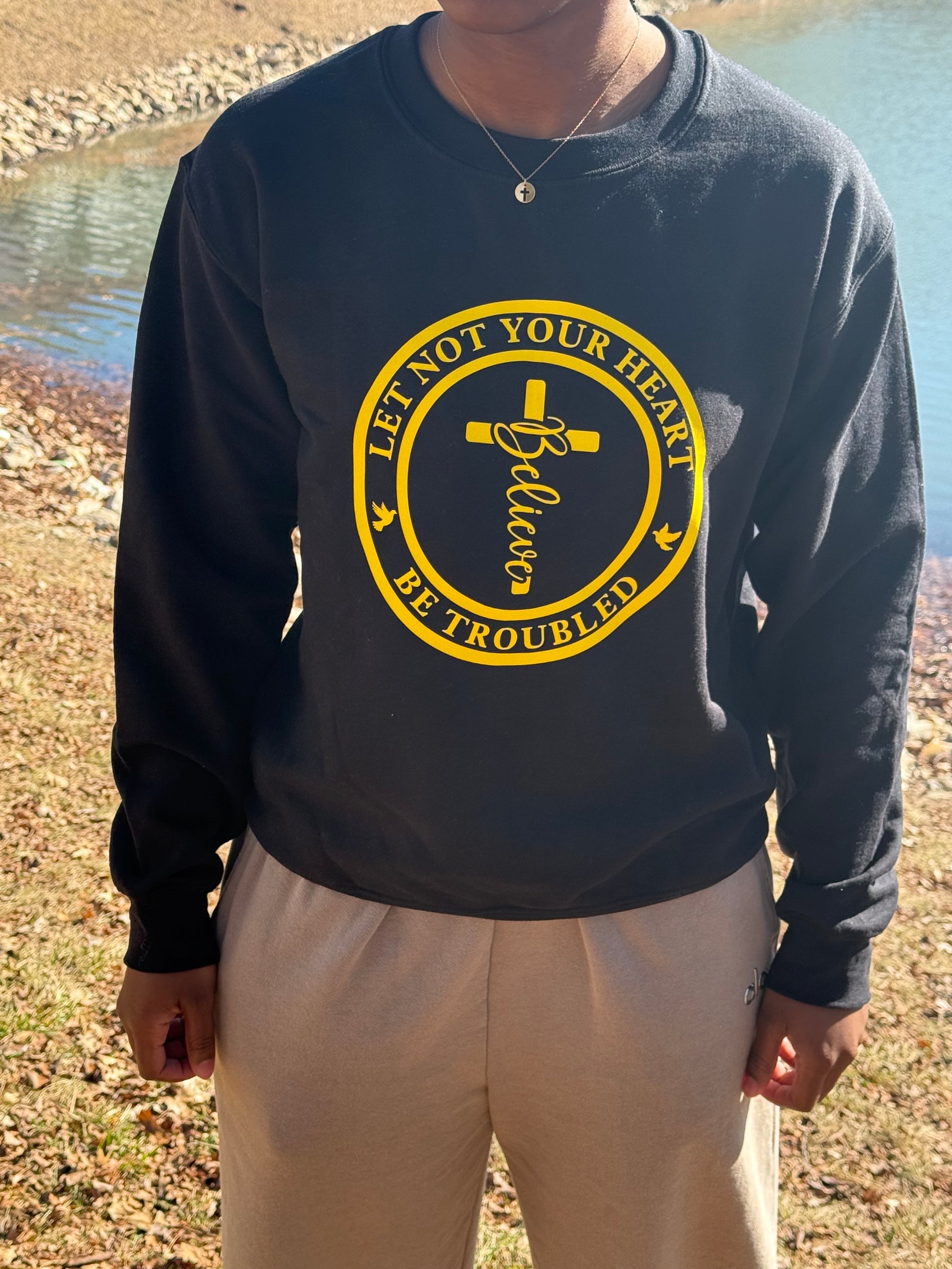 Person in black sweatshirt standing near grass and water, Roxzell