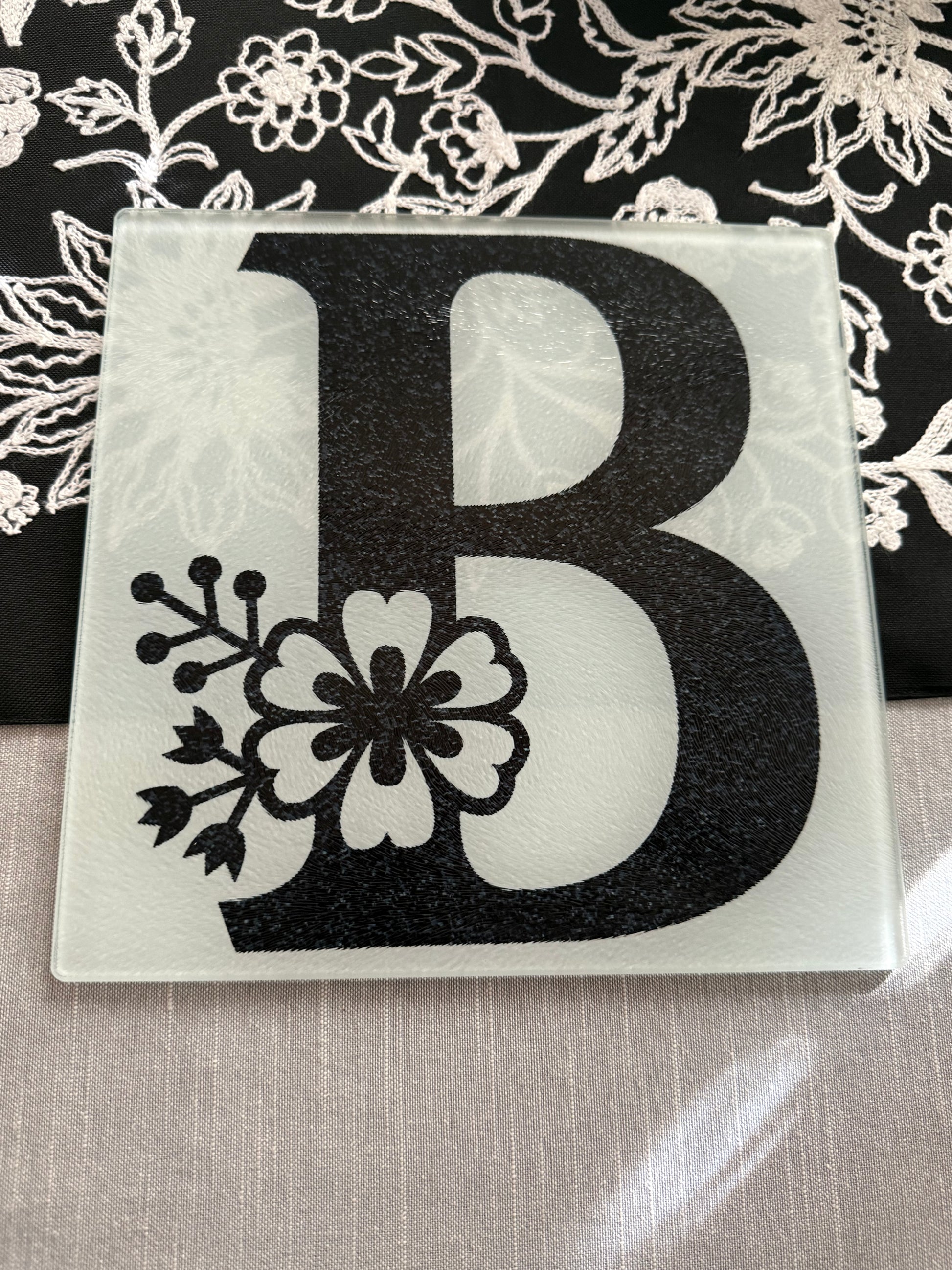 Personalized glass cutting board with uppercase "B" and integrated floral artwork on embroidered table runner, Roxzell