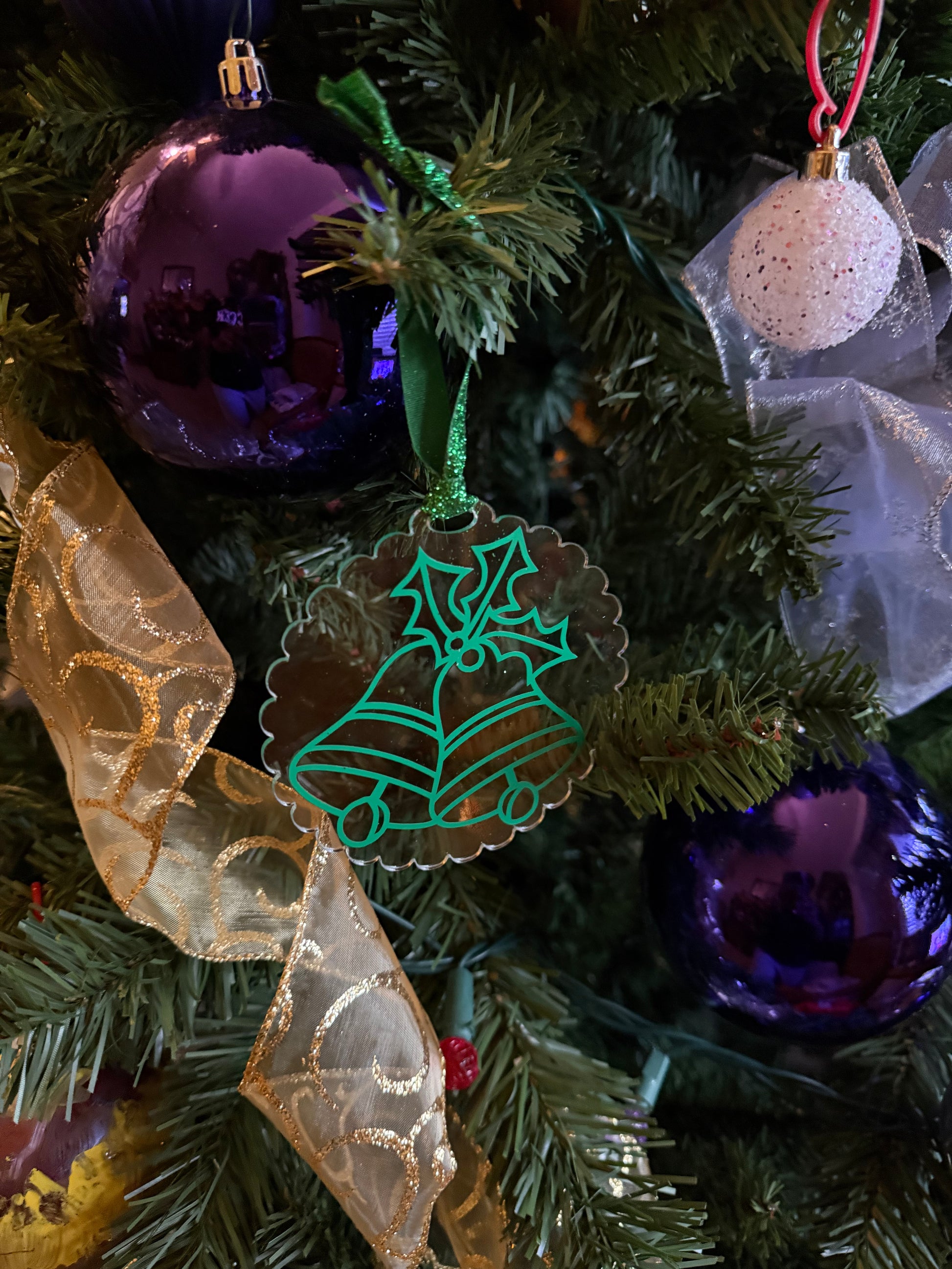 Festive ornament with scalloped edges and green glitter ribbon featuring bells and holly design on a Christmas tree.  Roxzell