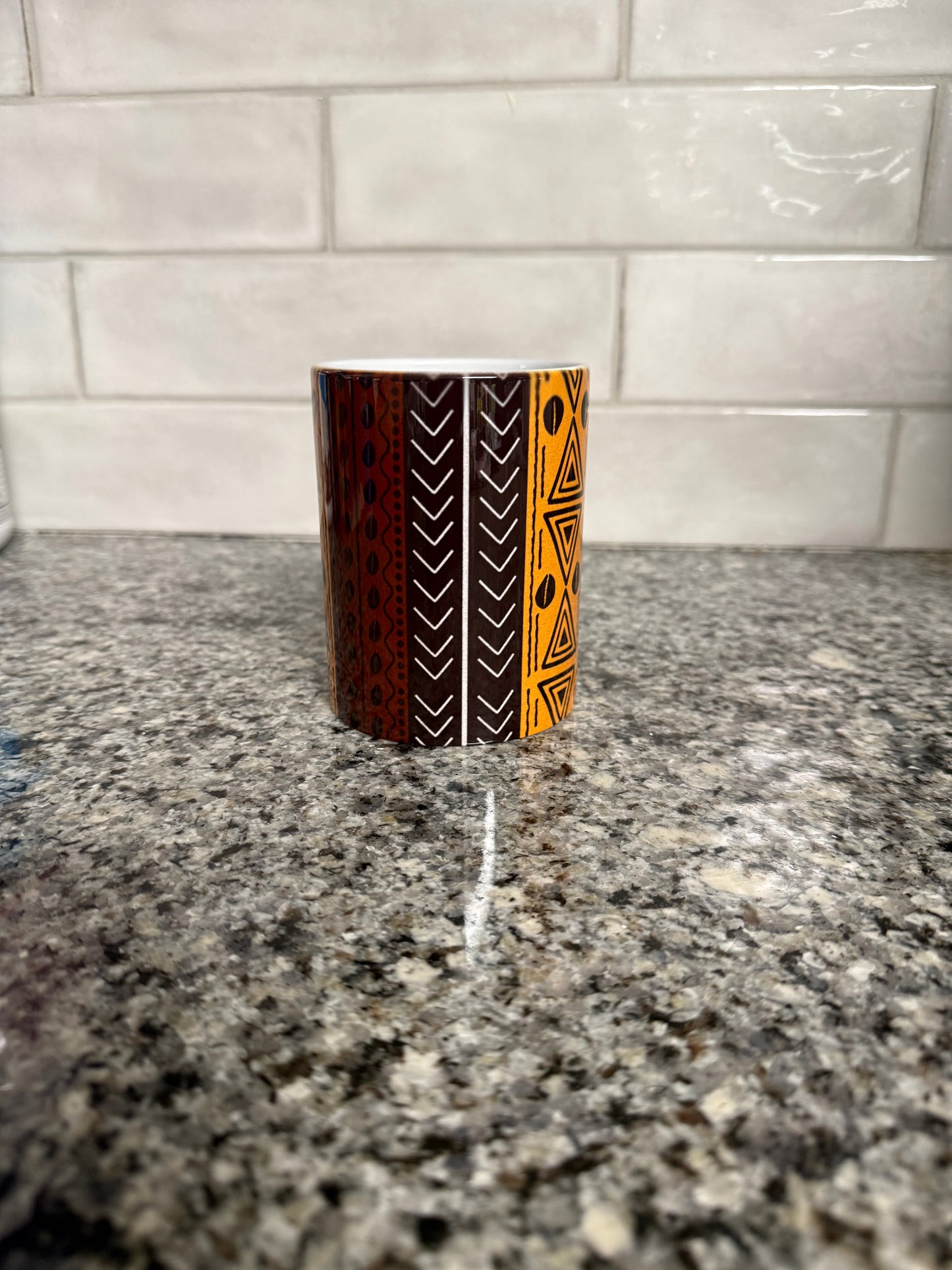 Ceramic mug with orange and brown tribal geometric patterns sitting on a granite countertop. Roxzell